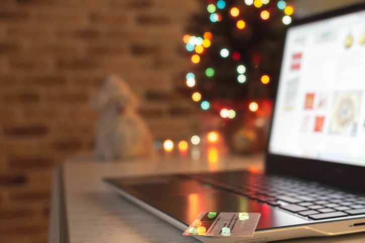 Holiday Tax Scams: ‘Tis the Season to be Wary Christmas shopping online. Laptop and credit bank card on table at home on the background of a Christmas tree with blurred bokeh lights.